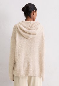 Pull beige avec capuche, présentant un design tricoté texturé et un ourlet côtelé. Le dos possède des détails sans couture et une coupe décontractée.