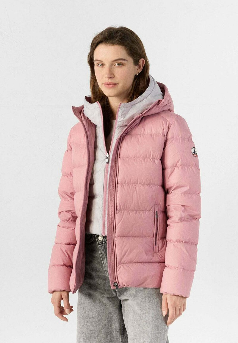 Veste doudoune rose clair avec une capuche grise, comportant des sections matelassées, une fermeture éclair à l'avant et des poches latérales. Texture lisse et design décontracté.