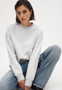 Grijze sweatshirt met een ronde halslijn en lange mouwen, gecombineerd met hooggenaaide blauwe jeans. Zachte textuur en een relaxte pasvorm.