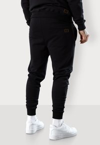 Schwarze Jogginghosen aus weichem Material, mit schlanker Passform, elastischem Bund, seitlichen Taschen und dezentem Logo-Detail in goldener Stickerei.