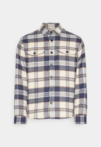 Camicia di flanella a quadri nei toni di crema, blu navy e arancio; presenta un colletto, due tasche sul petto e bottoni neri; maniche lunghe.