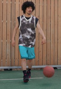 Košarkaš dribla loptu, nosi prugastu bezrukavnu dres u crno-bijeloj boji, tirkizne kratke hlače i crne sportske cipele.