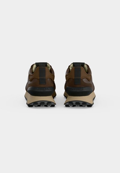 Paire de baskets marron et noir avec des semelles beige, vues de dos, montrant des grips de talon noirs texturés et des languettes de traction.