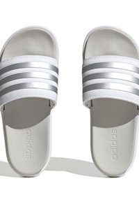 Adidas šlepetės su baltu sintetiniu paviršiumi, trimis metalizuotais sidabro juostelėmis, tekstūruotu padu ir iškilmingu logotipo spaudiniu ant pado.