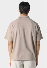 Koszula z krótkim rękawem w jasnym beżu, z teksturowanej tkaniny o luźnym kroju i płaskim kołnierzyku, z poziomym wzorem prążkowanym.