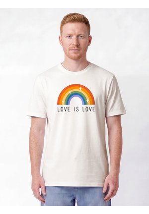 Man with red hair wears white t-shirt with rainbow and text "LOVE IS LOVE" standing against plain light background.