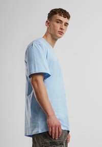T-shirt en coton bleu clair avec une coupe décontractée, des manches courtes et un col rond. Le tissu a une texture lisse avec des détails de conception minimaux.