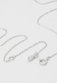 Collier délicat en chaîne d'argent avec un fermoir anneau à ressort et un pendentif géométrique pointu sur une surface lisse et claire.