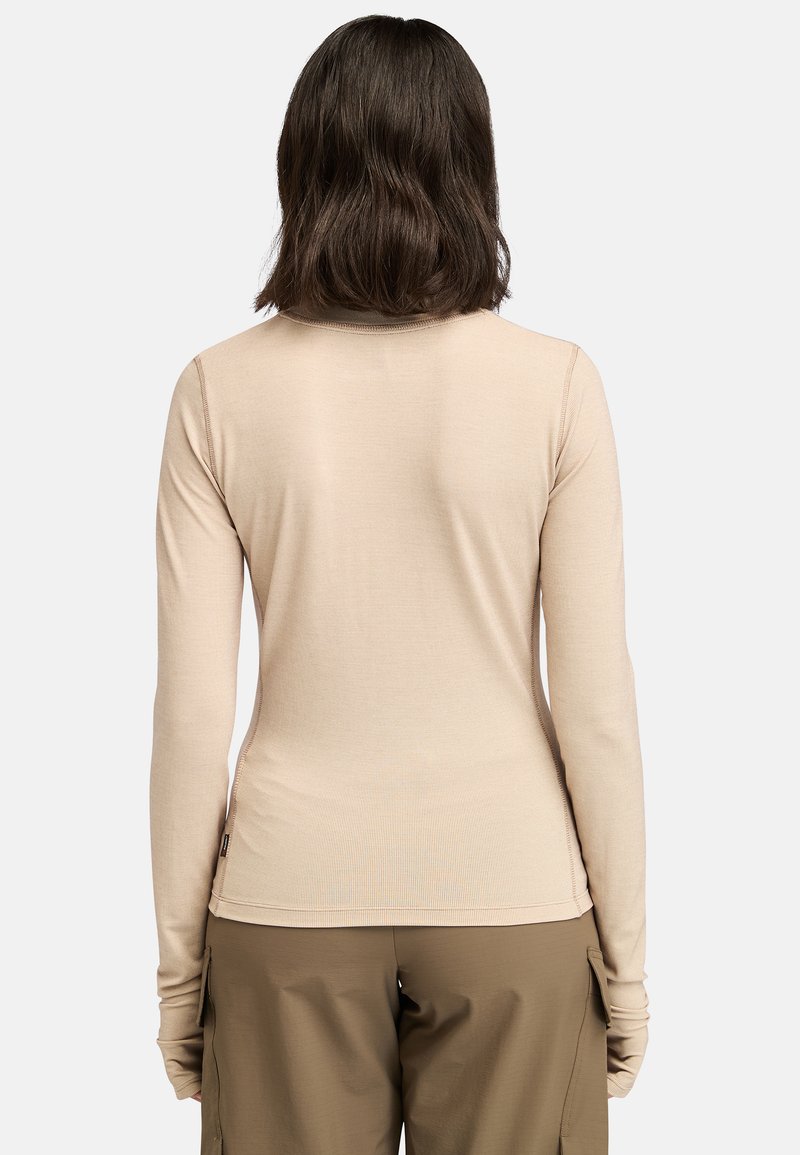 Maglia a maniche lunghe, aderente in tessuto a coste beige. Caratterizzata da un collo a giro e aperture per i pollici nei polsini, abbinata a pantaloni cargo beige larghi.