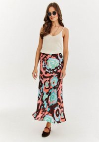 Dlhá, splývavá sukňa s živým abstraktným vzorom v ružovej, tyrkysovej a hnedej farbe, skombinovaná s ľahkým topom bez rukávov a okrúhlymi slnečnými okuliarmi.