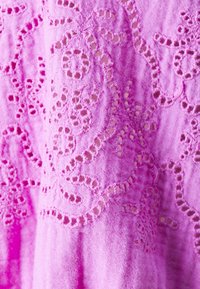 Tessuto rosa chiaro con dettagli in pizzo intricati, caratterizzato da motivi floreali e sezioni ritagliate, che mostrano una superficie morbida e testurizzata.