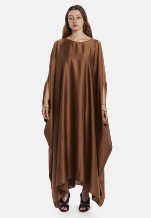 Kaftan en satin marron avec un col rond, des manches amples et des fentes latérales, offrant une silhouette fluide. Porté avec des sandales à talons noires.