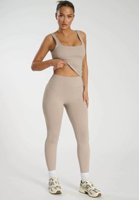 Beige atletisk crop top och högmidjade leggings, gjorda av stretchigt material, slät textur, figursydd design, kombinerat med kraftiga sneakers.