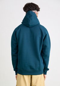 Felpa con cappuccio color verde petrolio scuro con collo alto e ampio cappuccio, caratterizzata da polsini e orlo a coste, realizzata in materiale morbido e strutturato.