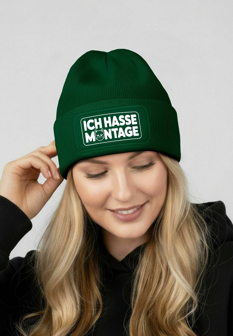 Green knit beanie with a structured design and a rectangular white patch featuring the text "ICH HASSE MONTAGE" and a cat graphic.