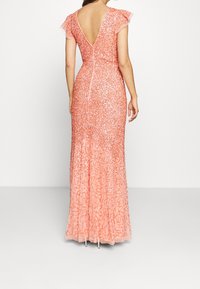 Růžová večerní toaleta se zdobením, s úzkým střihem, krátkými volánovými rukávy a hlubokým výstřihem na zádech, s jemným korálkovým zdobením a splývavou sukní.