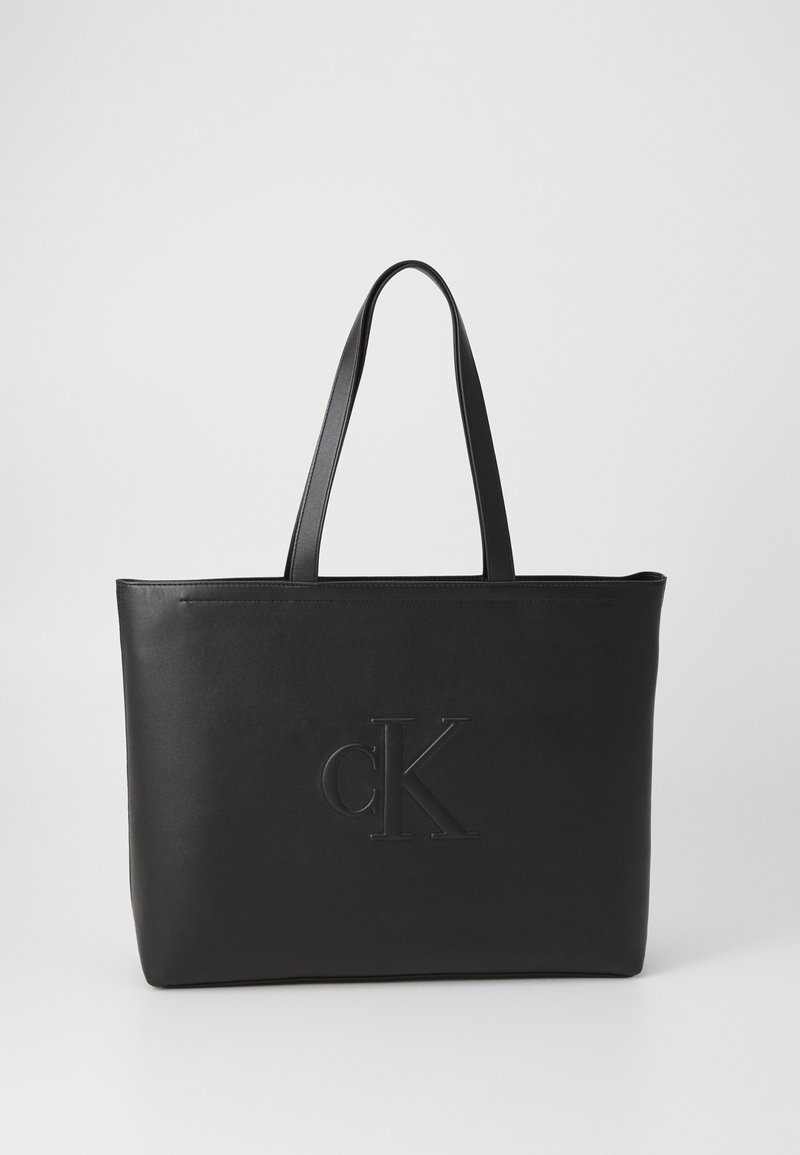 Črna usnjena torba s premazi s logojem "cK", ploske pravokotne oblike, dve trdni ročki, gladka tekstura, minimalističen dizajn.