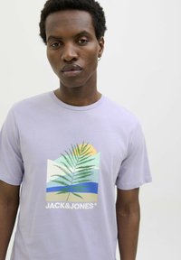 Camiseta de manga corta en color lila con un estampado gráfico de un helecho, sol y olas, con el nombre de la marca "JACK&JONES" en blanco.