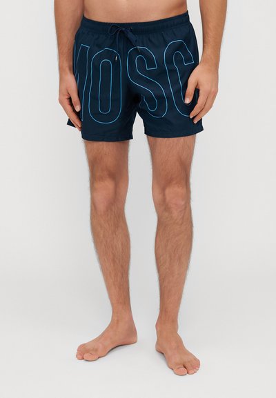 Shorts de bain bleu marine avec un grand texte "MOSC" en bleu clair. Ils possèdent une taille élastique avec cordon de serrage et sont fabriqués dans un matériau léger et lisse.