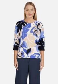 Pull en maille floral avec des motifs bleu, beige et noir. Caractéristiques d'un col rond et de manches trois-quarts avec des poignets côtelés.