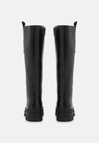 Černé vysoké kozačky z hladké kůže, s pevným podpatkem a zapínáním na zip vzadu. Vertikální švy dodávají tvar.