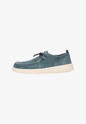 Scarpe in suede di colore teal con cuciture bianche, punta rotonda e suola in gomma crema. Presentano un design con lacci e una texture morbida.