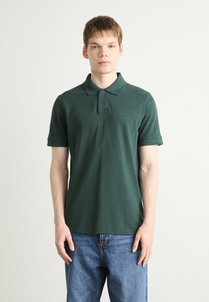 Dark green polo shirt made of soft fabric, featuring a collar, three buttons, and a subtle "BOSS" logo on the chest. Worn with blue jeans.