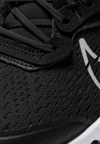 Svarta sportskor med en texturerad ovandel, släta svarta detaljer, snörningsdesign och en vit logotyp på sidan.