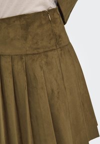Jupe en tissu suédé vert olive, avec des plis et une taille haute. Dotée d'une fermeture éclair sur le côté et d'une texture lisse. Pas de motifs ni d'accents visibles.