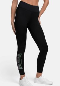 Black athletic leggings with a high waistband feature a printed "Lonsdale London" logo on the left leg, paired with white sneakers.