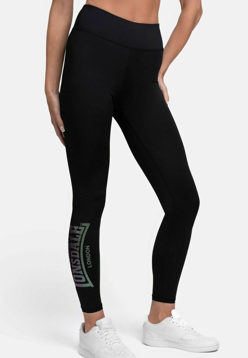 Fekete sportleggings, magas derékkal, a bal lábon a "Lonsdale London" felirattal, fehér sportcipőkkel párosítva.