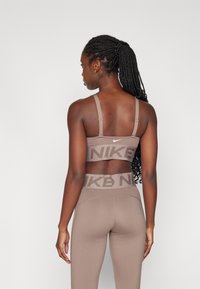 Nike sportski grudnjak i tajice u svijetlosmeđoj boji, s širokim brendiranim pojasom, podesivim trakama i glatkom teksturom.