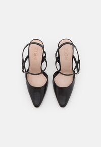 Černé kožené lodičky na vysokém podpatku s špičatou špičkou, s otevřeným designem a zkříženými kotníkovými řemínky se stříbrnou sponou.