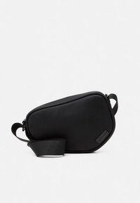 Juoda rankinė per petį, pagaminta iš lygaus sintetinio audinio, pasižyminti išlenktu dizainu, užtrauktuko uždarymu ir reguliuojama dirželio juosta patogumui.