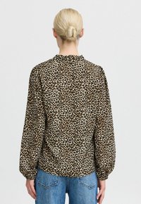 Leopard print blouse with a gathered neckline, long puffed sleeves, and soft fabric; paired with blue denim jeans.