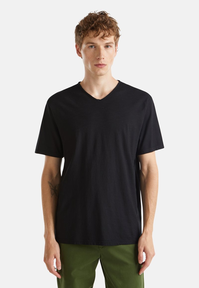 Camiseta negra de cuello en V y mangas cortas, hecha de una tela suave. Presenta un corte relajado y un diseño minimalista, combinada con pantalones verdes.