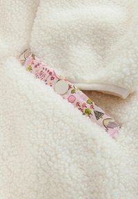 Țesătură moale de lână de culoare crem, cu o bandă decorativă cu model floral roz și închidere cu capse albe integrată în design.