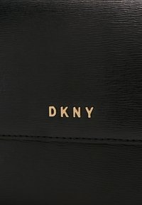 Portafoglio in pelle nera con finitura testurizzata e logo "DKNY" in oro stampato. Cuciture dettagliate visibili lungo i bordi.