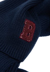 Tumši zils adīts cepures modelis ar faktūras ribām un bordo izšūtu burtu "B" uz sāna. Mīksts un elastīgs materiāls.