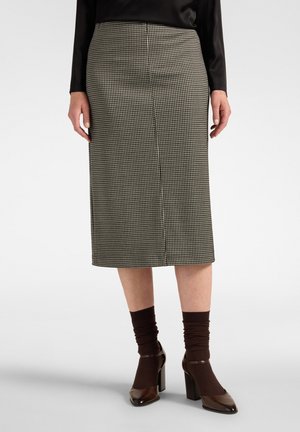 Donna che indossa un top nero, gonna pied de poule al ginocchio, calzini marrone scuro e scarpe Mary Jane marroni con tacco largo.