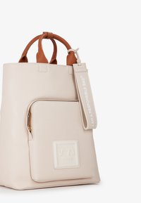 Borsa tote in pelle beige con manici marroni, tasca frontale con cerniera e un'etichetta che dice "IO SONO UNA BORSA RESPONSABILE".
