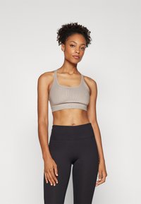 Light taupe sports bra with a textured design, wide straps, and a mid-rise band. Paired with high-waisted black leggings, smooth texture.