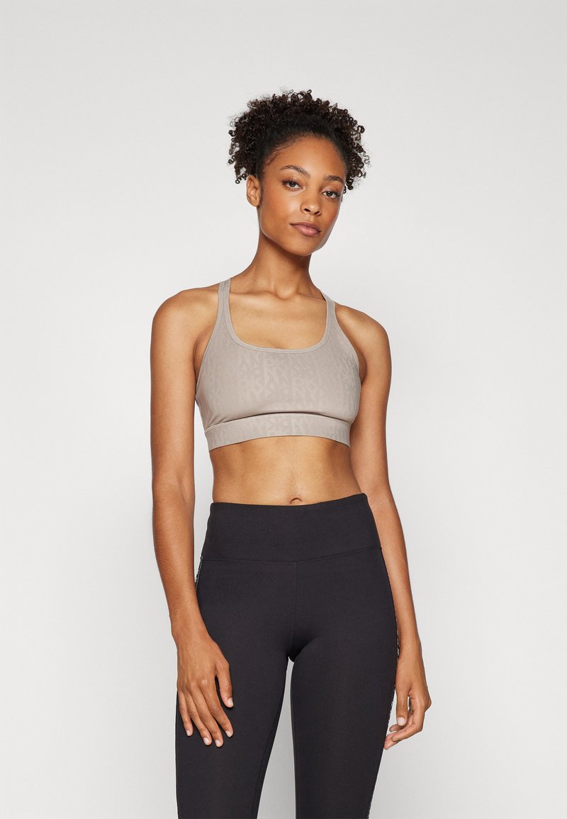Light taupe sports bra with a textured design, wide straps, and a mid-rise band. Paired with high-waisted black leggings, smooth texture.