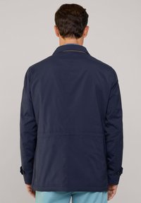 Giacca navy con una texture liscia e una vestibilità su misura, caratterizzata da un colletto classico, polsini abbottonati e un design semplice sul retro.