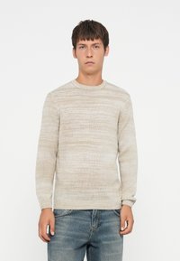 Jasny beżowy sweter o teksturowanym, paskowanym wzorze. Ma okrągły dekolt i długie rękawy, zestawiony z dżinsami.