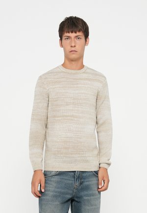 Lys beige genser med en teksturert, stripete design. Har rund hals og lange ermer, sammen med denimjeans.