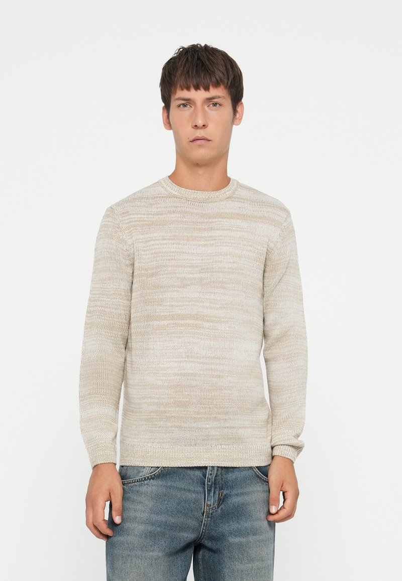 Lys beige genser med en teksturert, stripete design. Har rund hals og lange ermer, sammen med denimjeans.