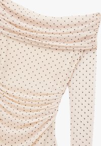 Blusa de manga larga y hombros al aire en tela beige claro con lunares marrones; presenta textura fruncida y diseño drapeado.