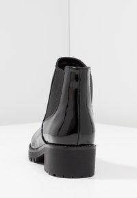 Černé lakované kozačky ke kotníkům s elastickými bočními panely a robustním černým podpatkem. Podešev má texturovaný vzor pro lepší přilnavost.