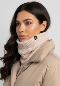 Beige knitted neck warmer with a ribbed texture, featuring a black brand tag on the side, worn over a light-colored puffer jacket.